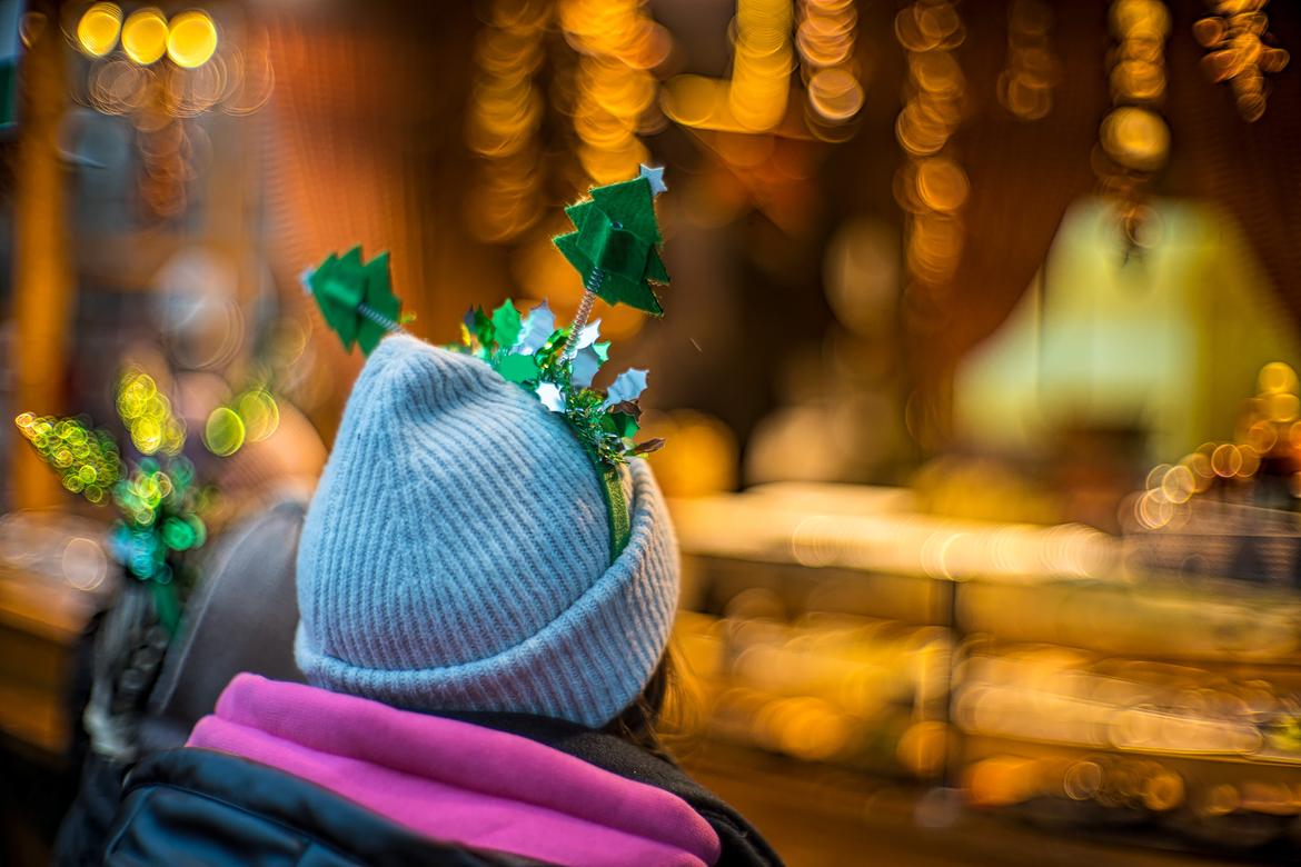 Frauenkopf von hinten mit Mütze und aufgestecktem Weihnachtsbaumschmuck vor Weihnachtsstand